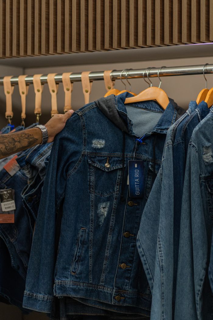Close-up of various denim jackets hanging on wooden hangers in a clothing store.